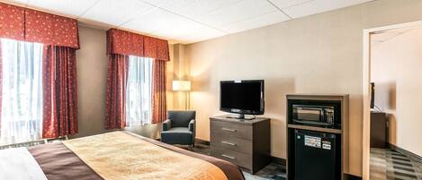 Una habitación de hotel con cama, televisión, refrigerador pequeño y escritorio con lámpara.