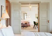 A hotel room with a bed, a sitting area with a sofa and chairs, a dining table, and a chandelier.
