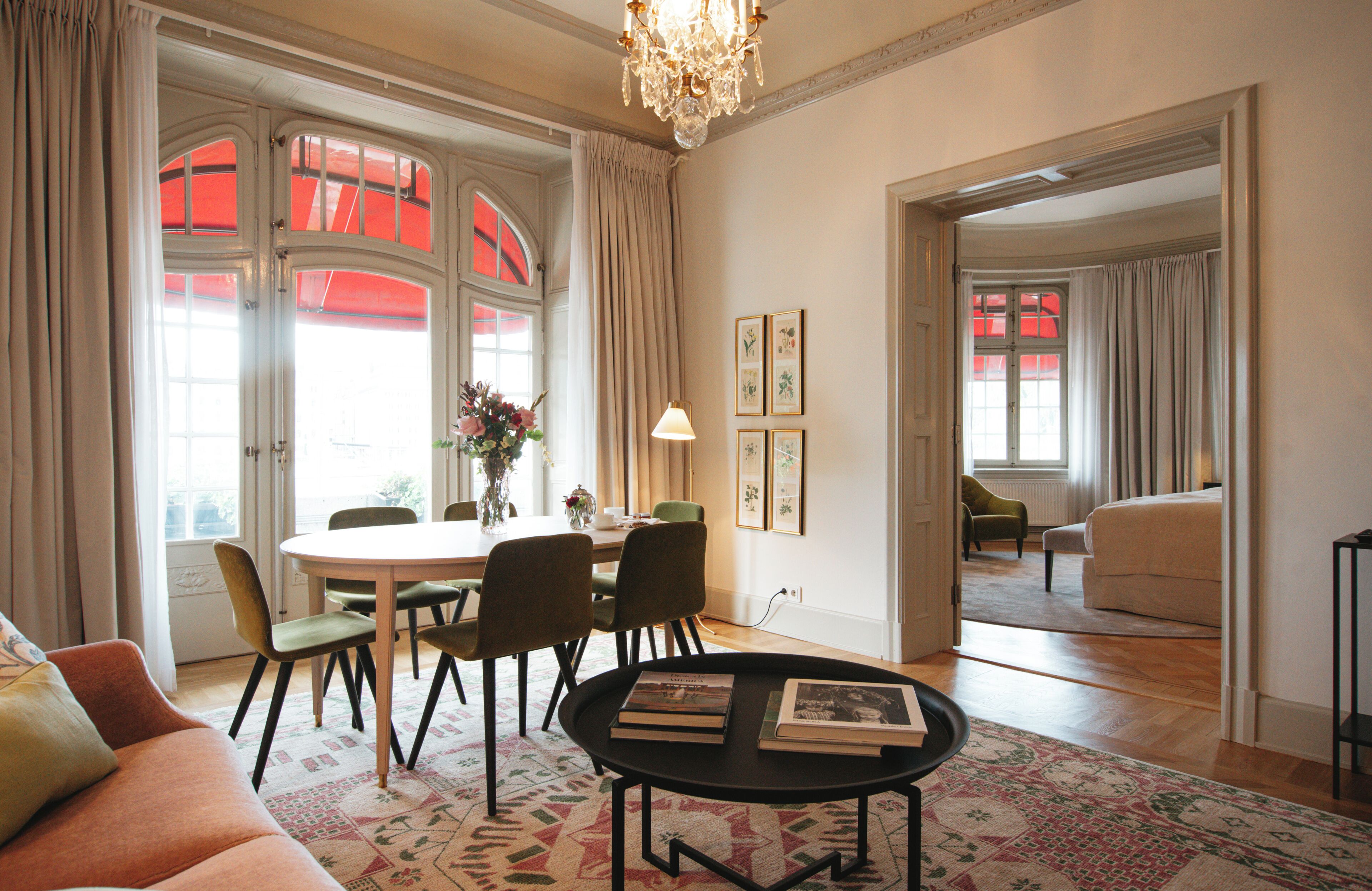 A spacious living room with a dining area, a chandelier, and a view through an open door.