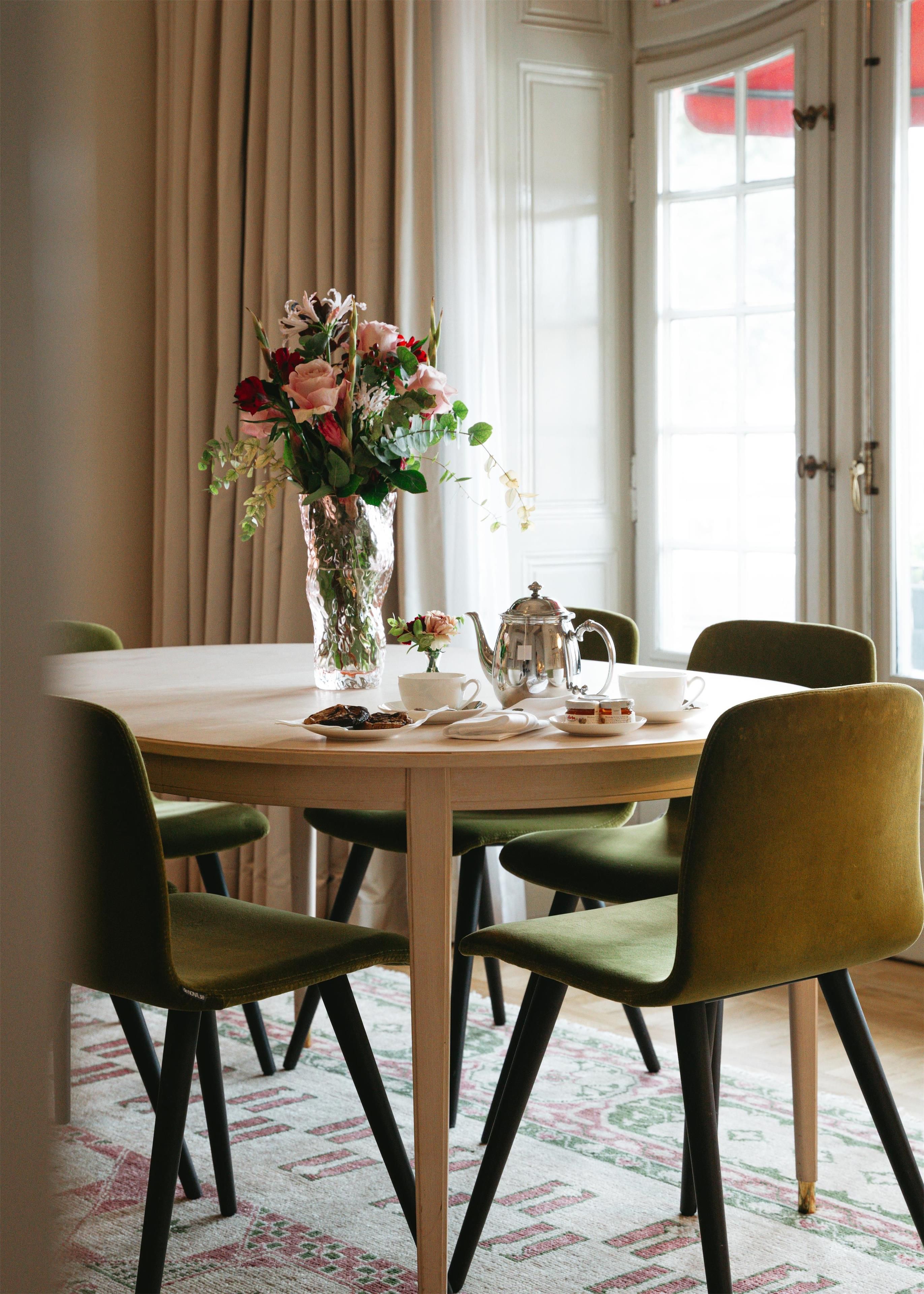 A dining table with a vase of flowers, a teapot, cups, and a plate of food.