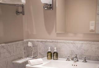 A bathroom with a white sink, marble walls, a towel rack, a glass soap dispenser, and a tissue box.