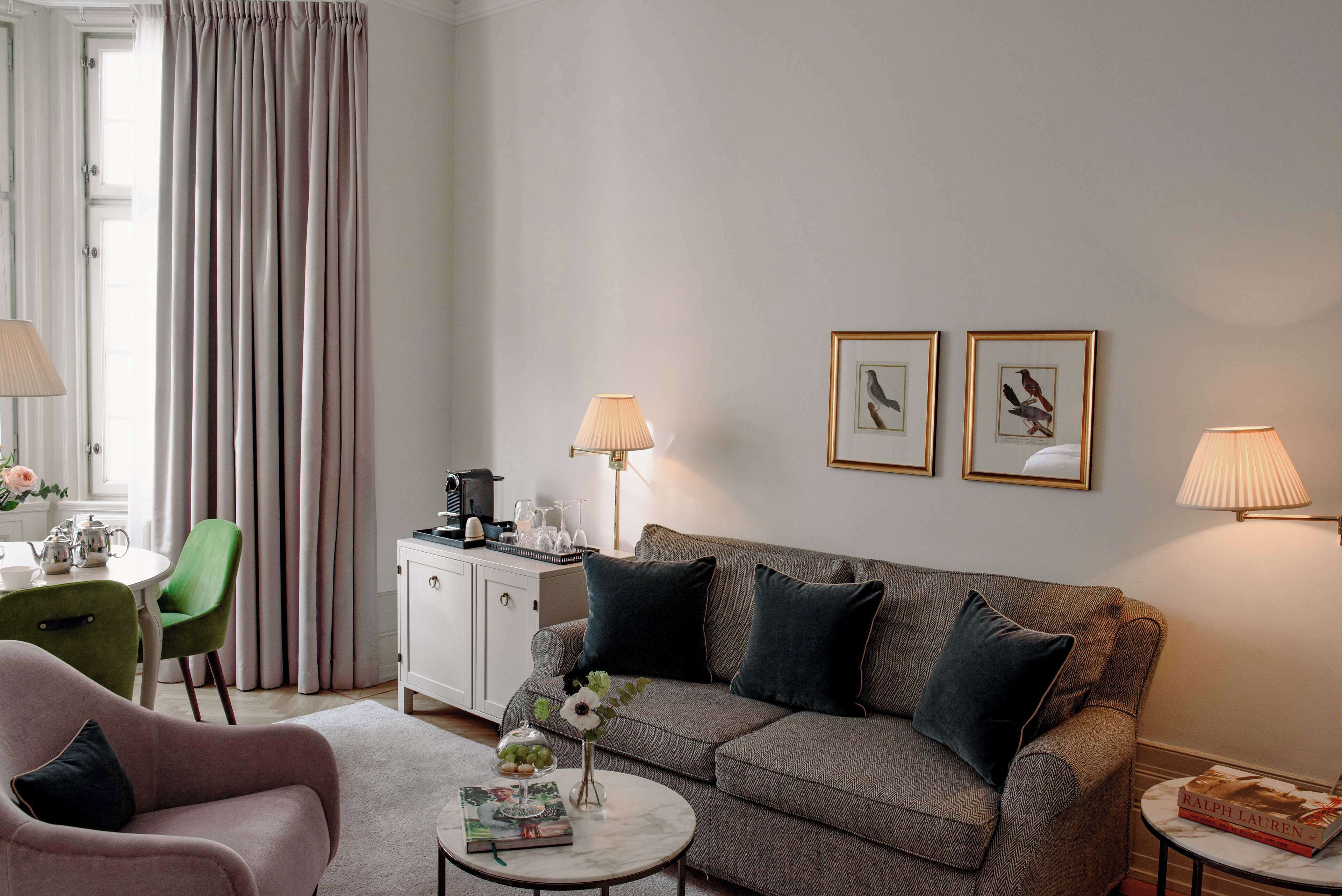 Un salon moderne comprenant un canapé, un fauteuil, une table basse et un coin repas avec une table et des chaises. Des tableaux encadrés ornent le mur, et une lampe est placée de chaque côté du canapé.