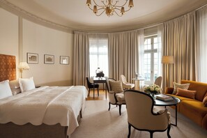 A hotel room with a large bed, a sofa, a dining table with chairs, and a chandelier.