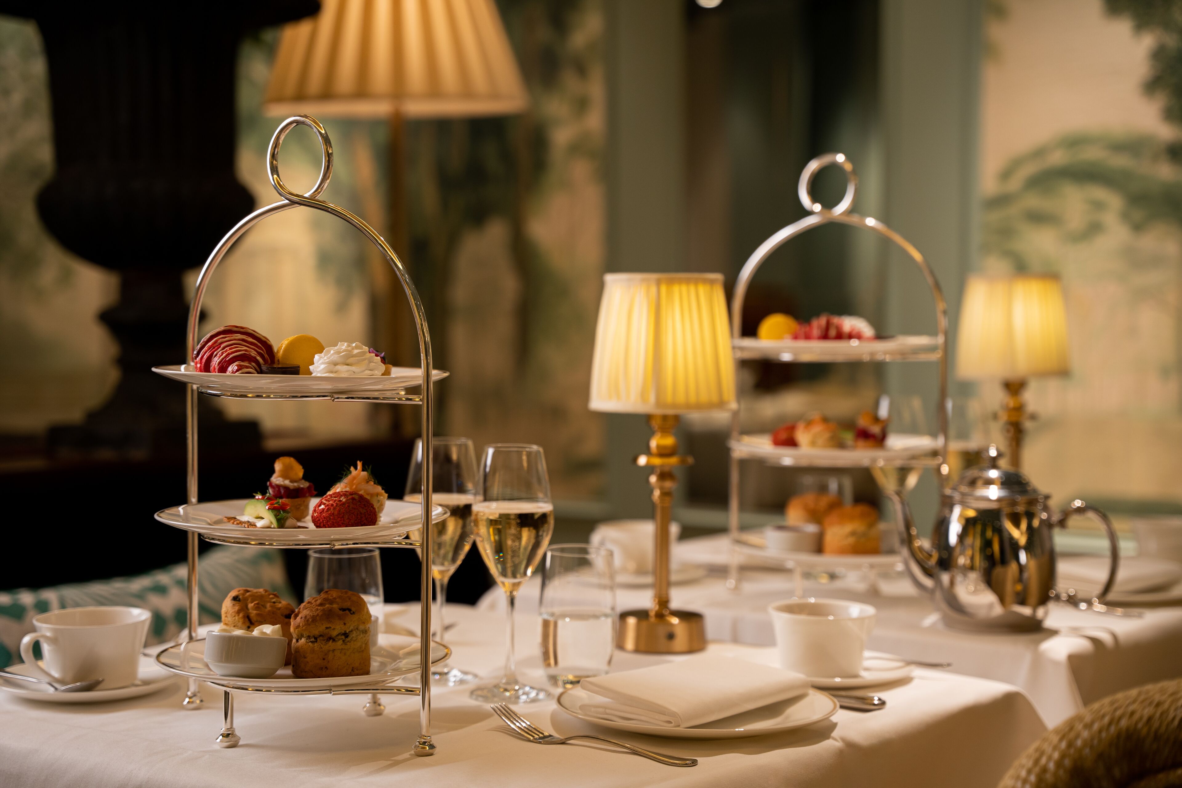 A formal dining setup with tiered tea and dessert stands, elegant table settings, and ambient lighting.