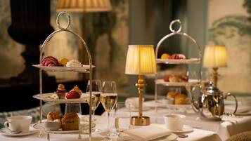 A formal dining setup with tiered tea and dessert stands, elegant table settings, and ambient lighting.