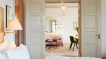 A hotel room with a bed, a round table, a sofa, a chair, a chandelier, and a mirror.