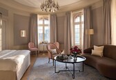 A hotel room with a bed, a sofa, a coffee table with a vase of flowers, and a chair.