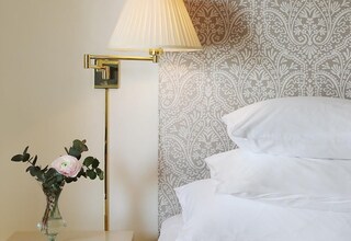 A neatly made bed with white linens, a bedside lamp, and a small table with a vase of flowers.