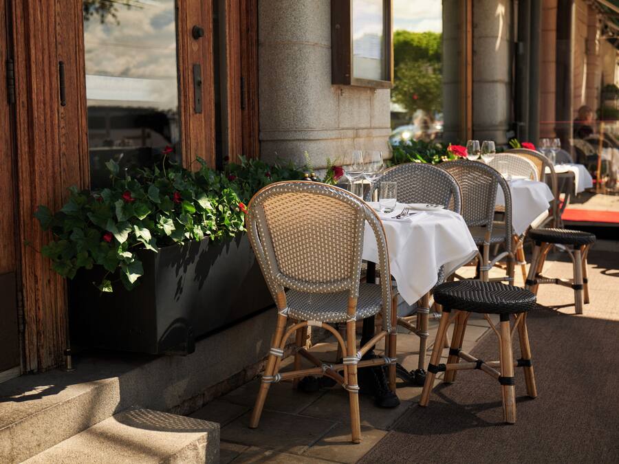 Un espacio de comedor al aire libre con sillas y mesas de mimbre, un macetero con plantas y un pilar de piedra.