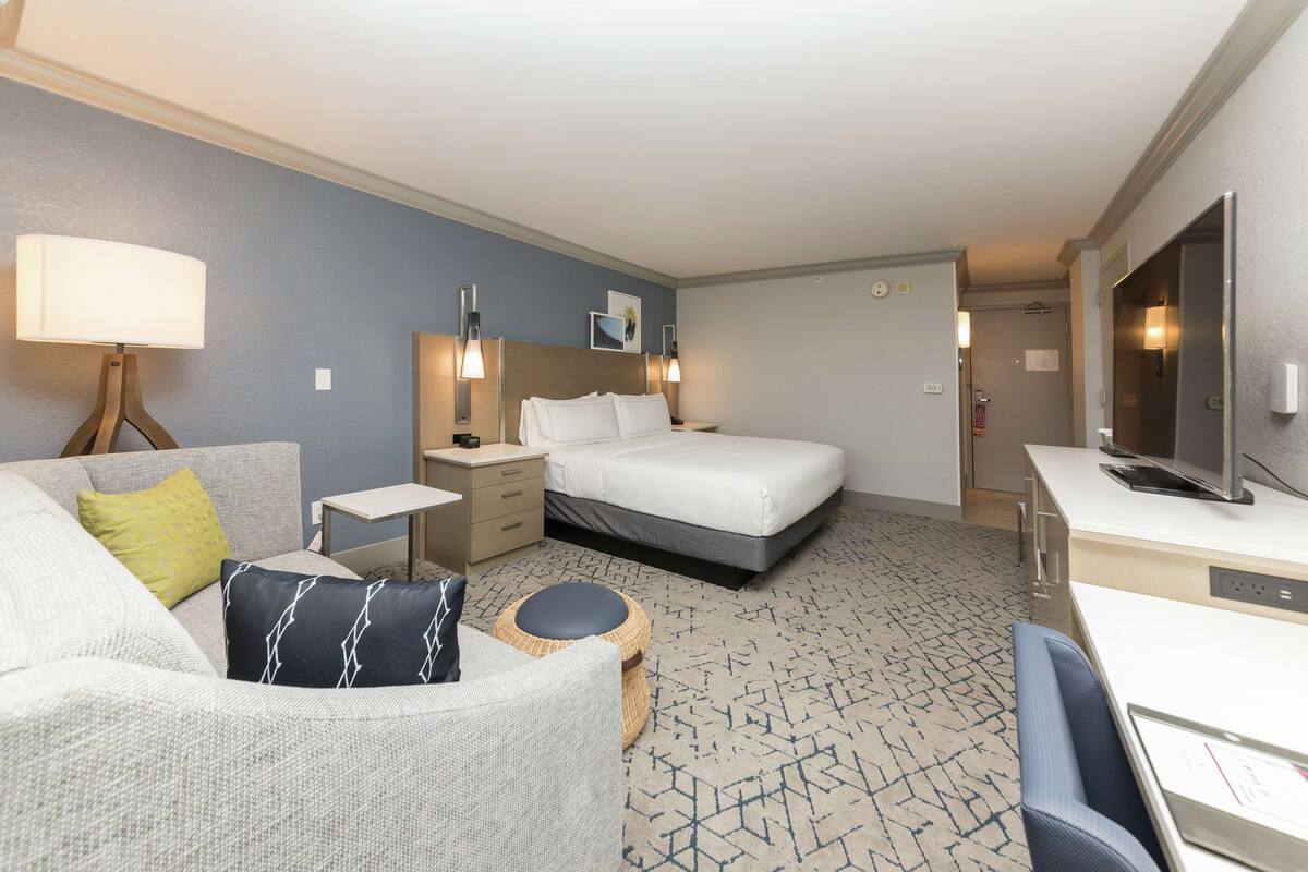 A hotel room with a bed, a sofa, a small table, a TV, and a desk.