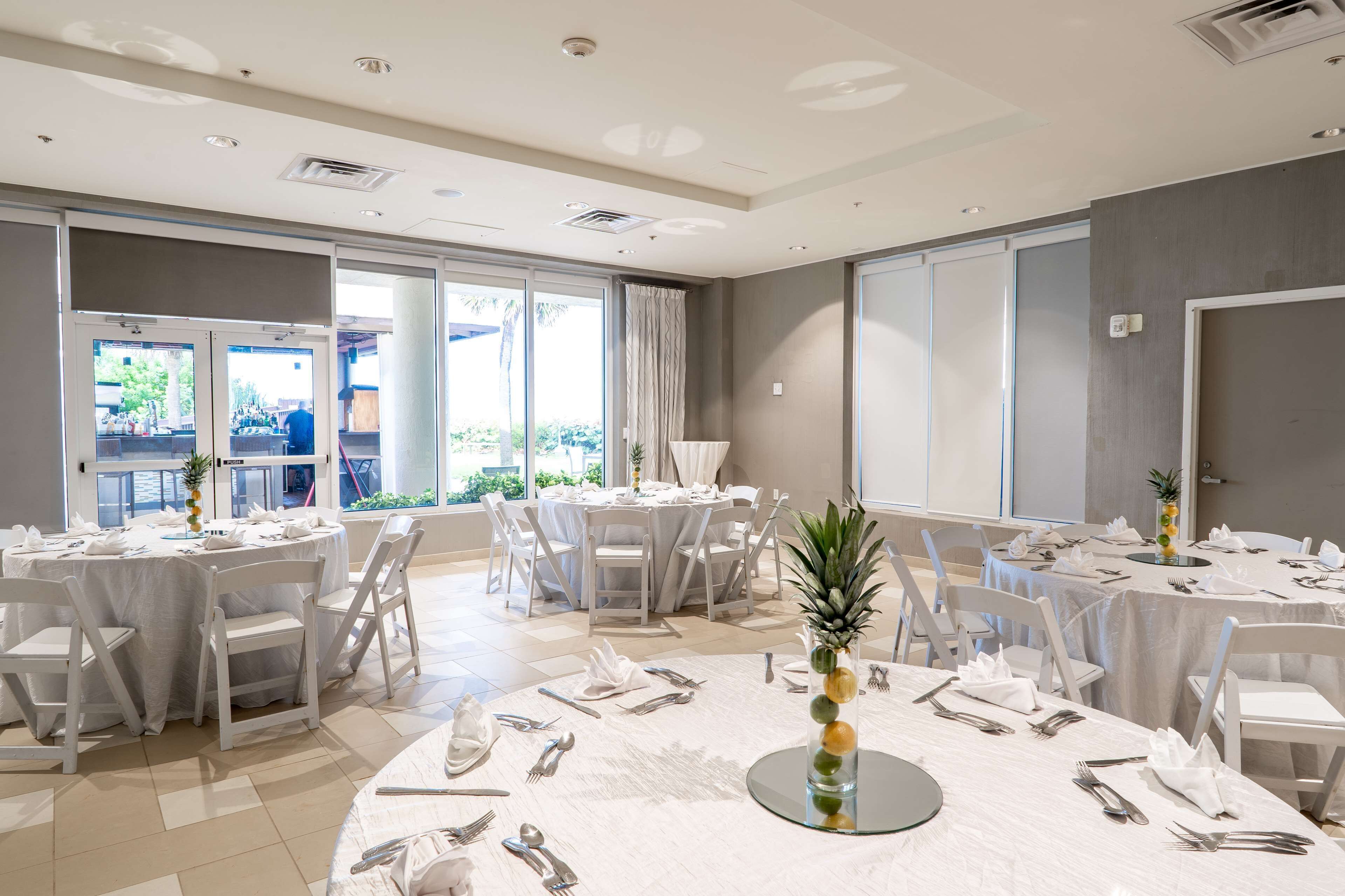 Un comedor amplio con mesas redondas dispuestas para una comida, ventanas grandes y vistas al exterior.