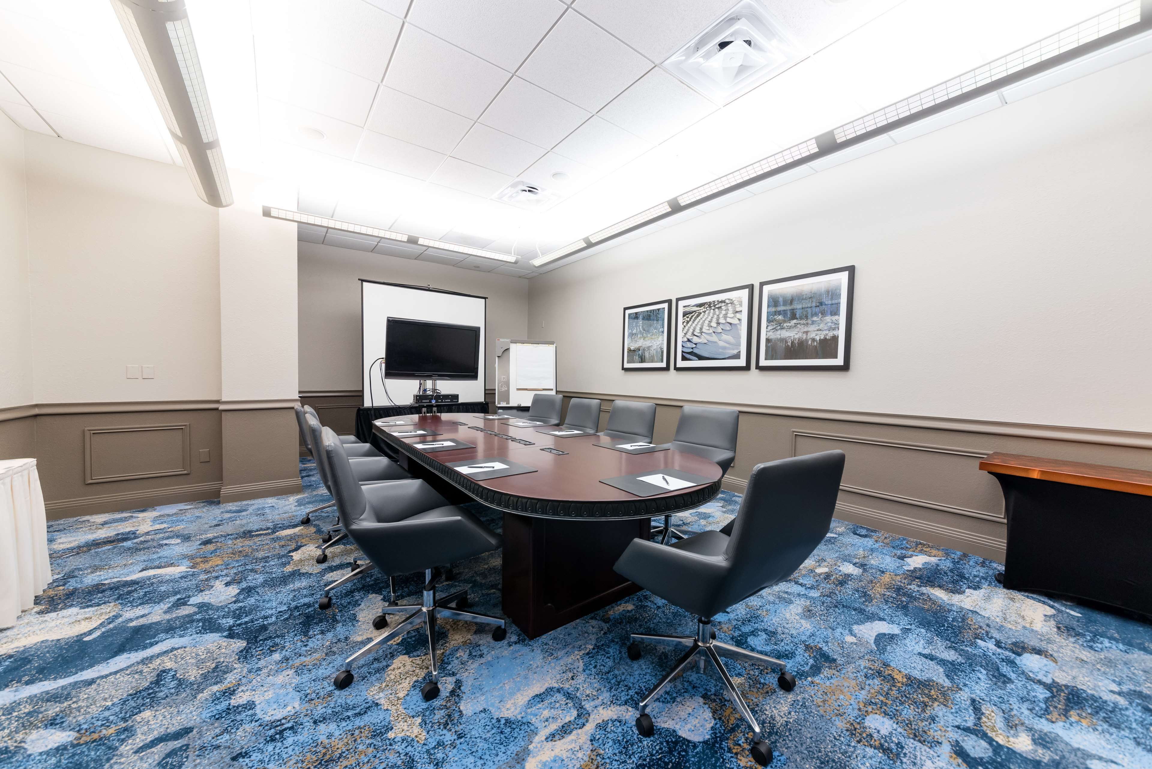 A conference room with a large table, chairs, a whiteboard, and framed pictures on the wall.