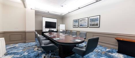 A conference room with a large table, chairs, a whiteboard, and framed pictures on the wall.