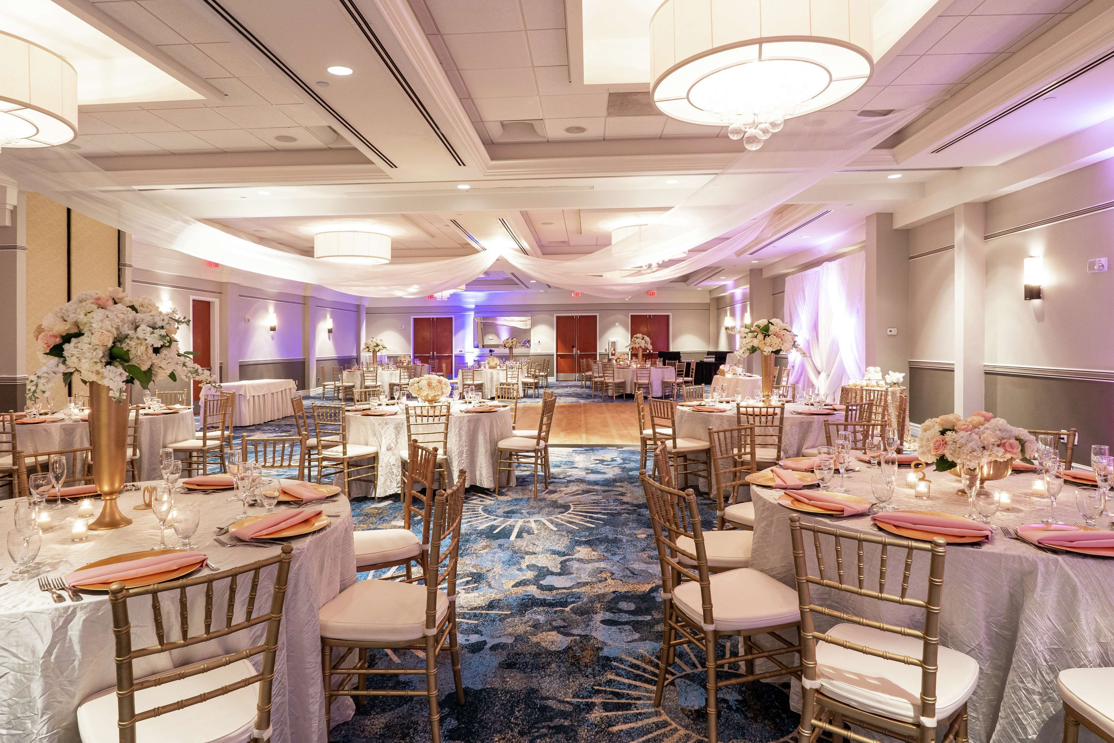 A banquet hall with round tables, chairs, and floral centerpieces.