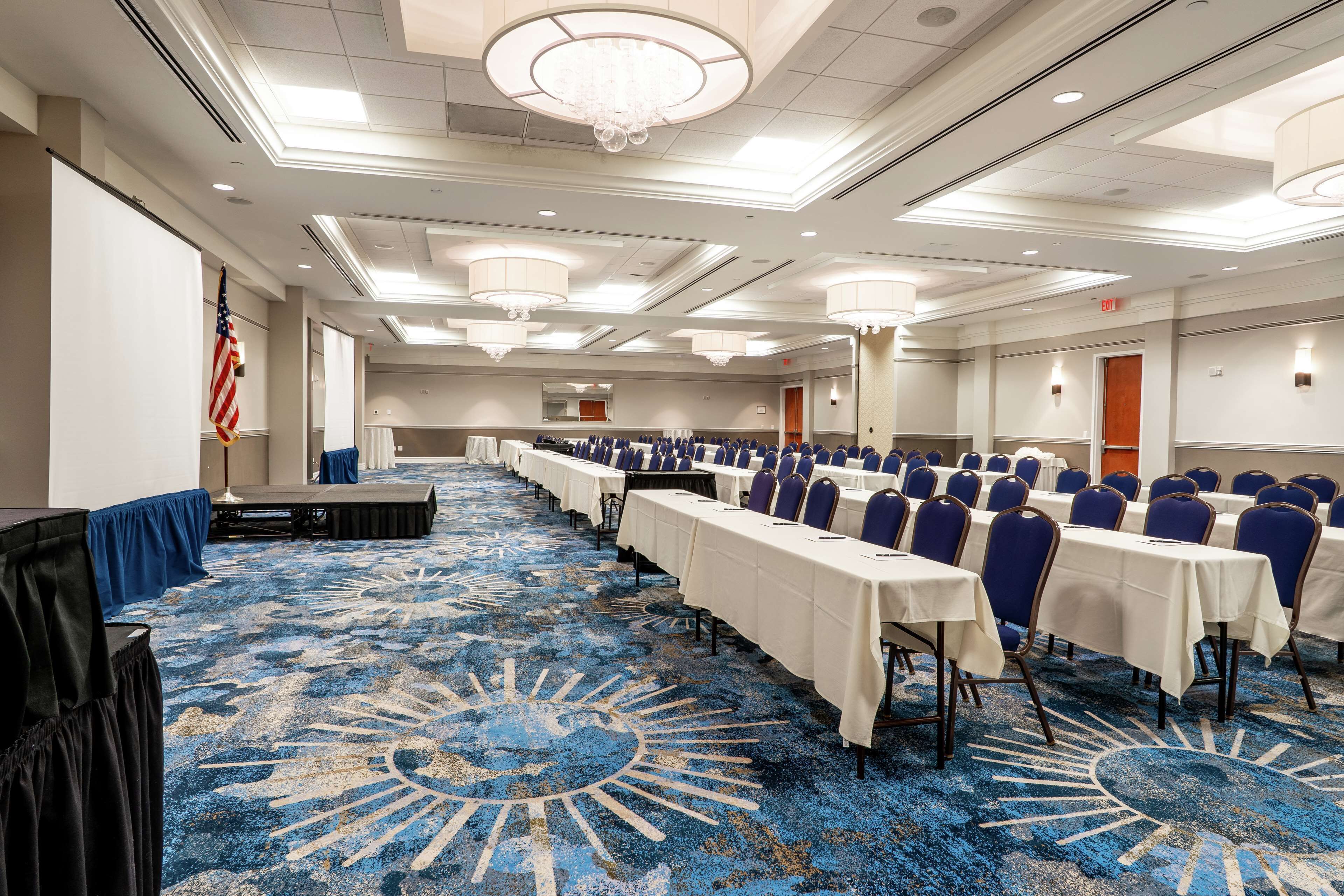 A conference room with rows of tables and chairs, a patterned carpet, and a chandelier.