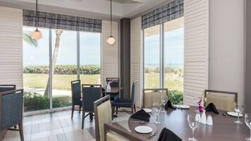 A dining area with a table set for four, large windows with a view of the outdoors, and a hanging light fixture.