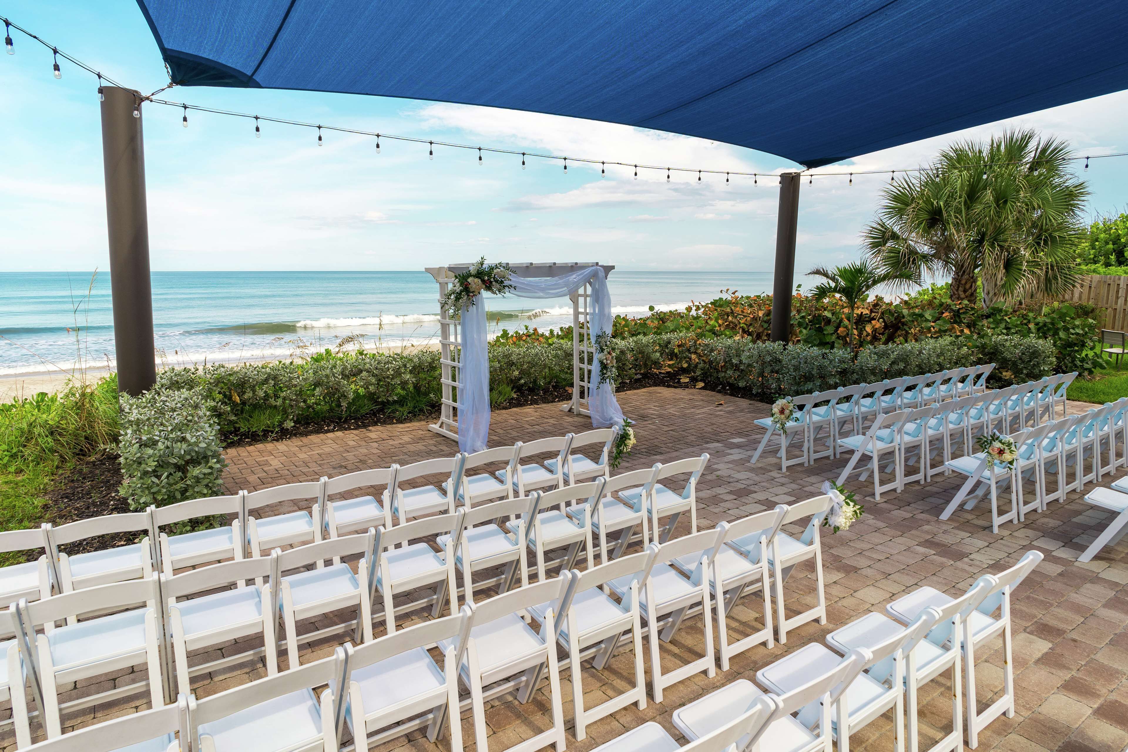 An outdoor wedding venue with white chairs arranged in rows, a white arch with floral decorations, and a view of the ocean.