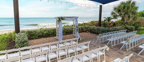 An outdoor wedding venue with white chairs arranged in rows, a white arch with floral decorations, and a view of the ocean.