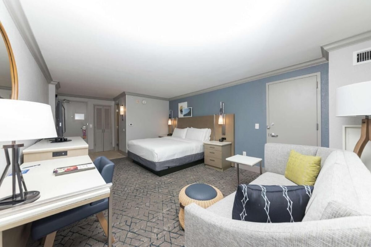 Una habitación de hotel con cama, escritorio, silla, sofá y una pequeña mesa redonda.