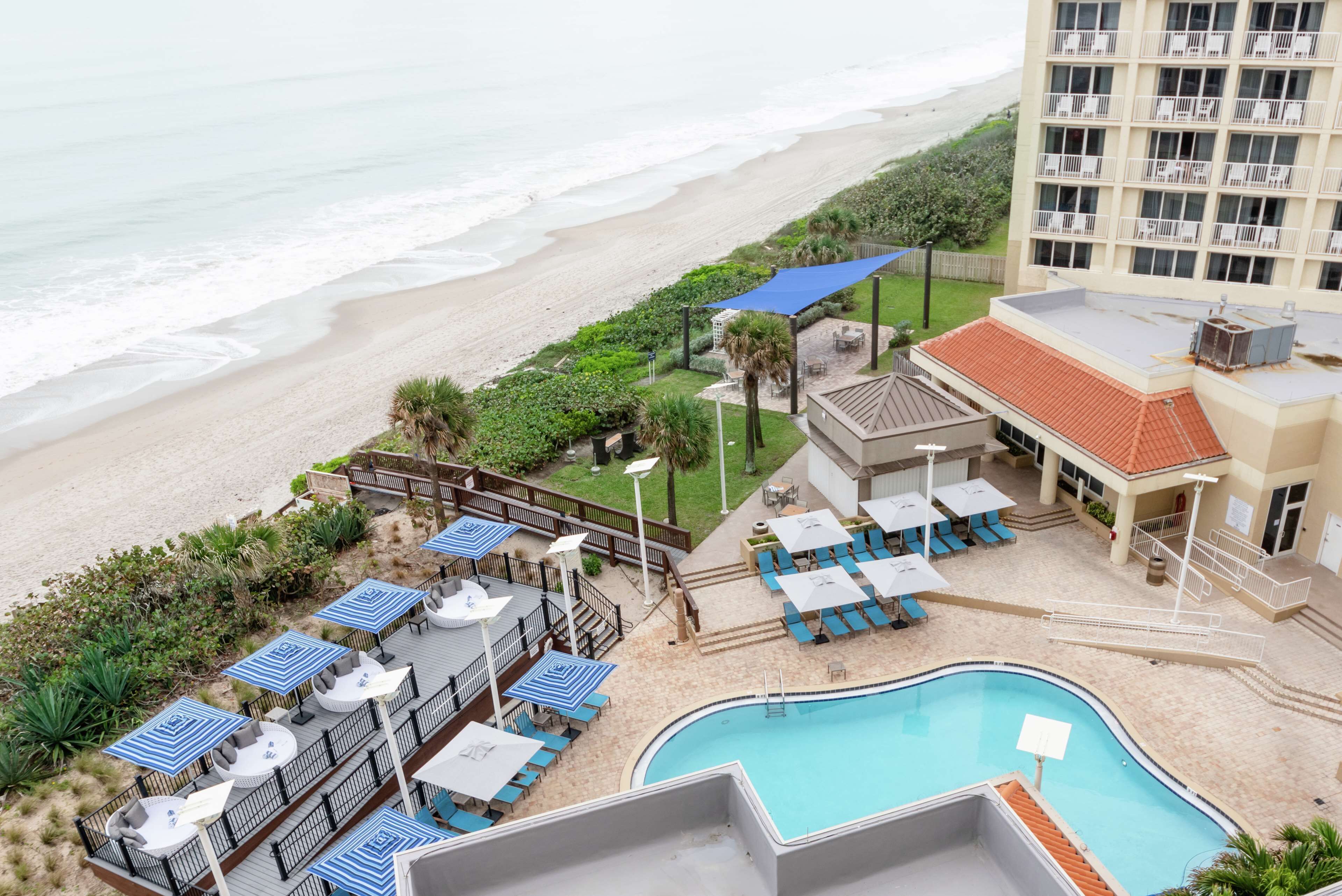 A hotel with a pool, beach view, and outdoor seating area.