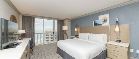 A hotel room with a large bed, a desk with a computer, a TV, and a balcony with a view.