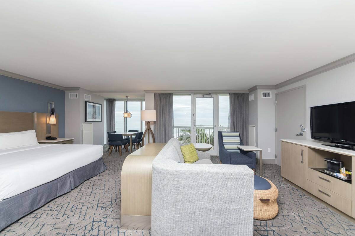 A hotel room with a large bed, a sofa, a desk, a television, and a view of the outdoors.