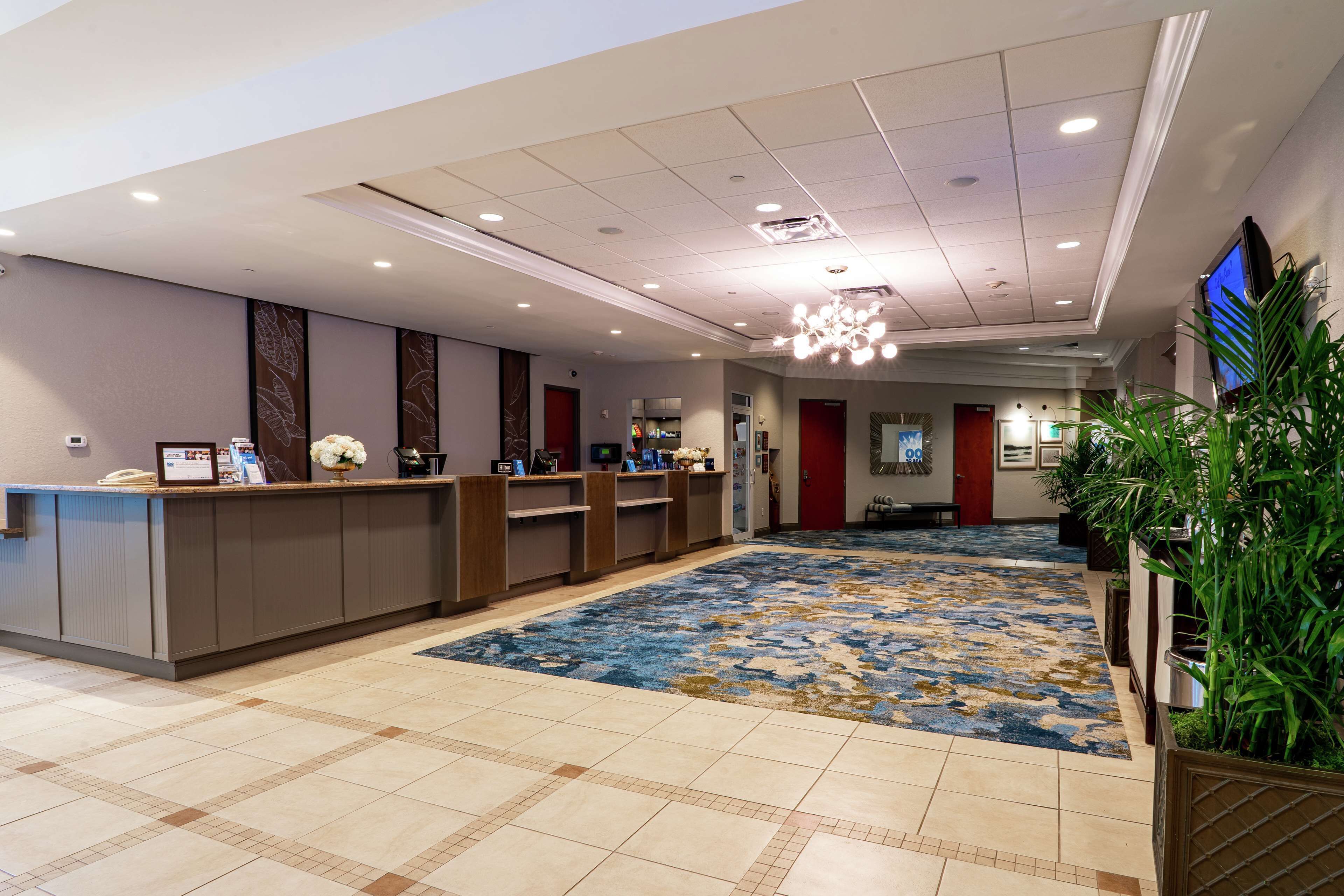 A hotel reception area with a reception desk, a blue patterned carpet, and a television screen on the wall.
