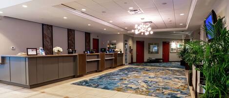 A hotel reception area with a reception desk, a blue patterned carpet, and a television screen on the wall.