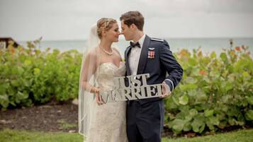 A couple holding a sign that says "JUST MARRIED" in front of a garden with a view of the sea.