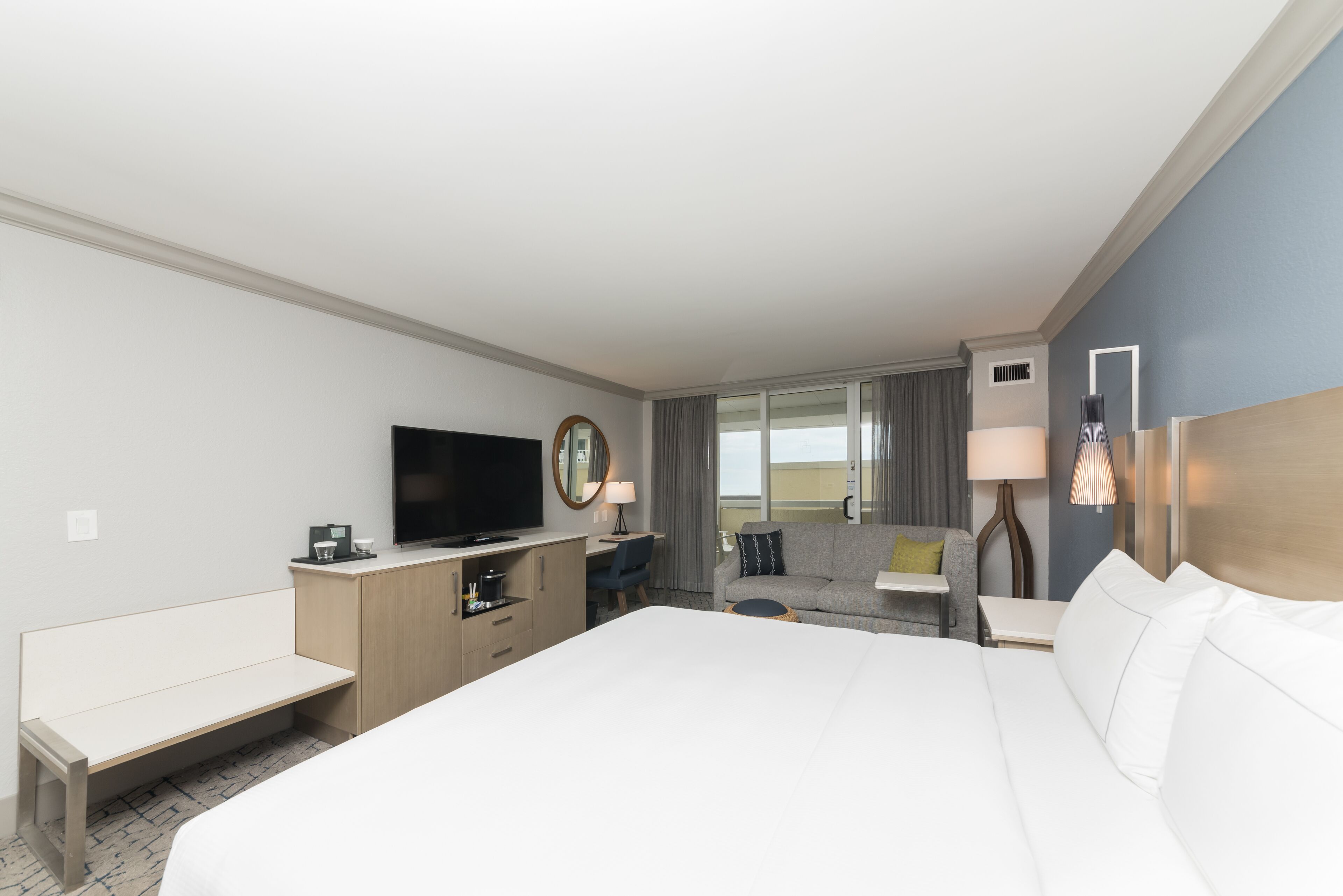 Habitación de hotel con una cama grande, un escritorio con televisor de pantalla plana, un sofá, una silla y una mesita.