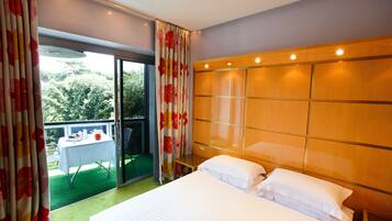 Una camera d'albergo con un letto grande, una testiera in legno, un tavolino e un balcone con tavolo e sedie.