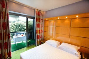 Una camera d'albergo con un letto grande, una testiera in legno, un tavolino e un balcone con tavolo e sedie.