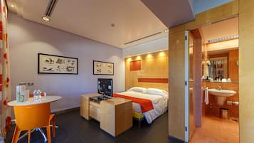 A modern hotel room with a bed, a desk, and a bathroom.