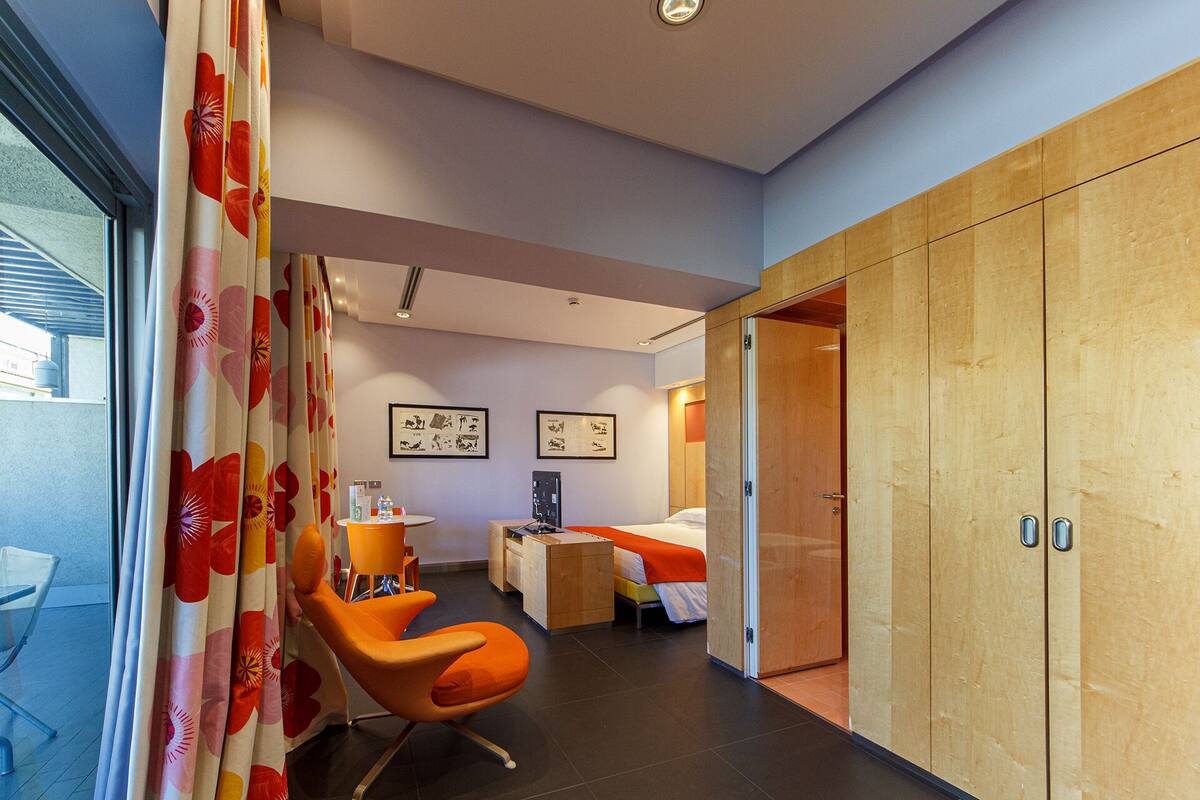 A modern hotel room with a bed, a desk, a chair, and a wardrobe.