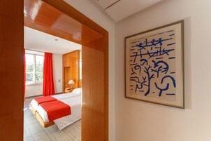 Una camera d'albergo con un letto, un comodino, una lampada e una finestra con tende rosse. Sul muro è presente un quadro incorniciato.