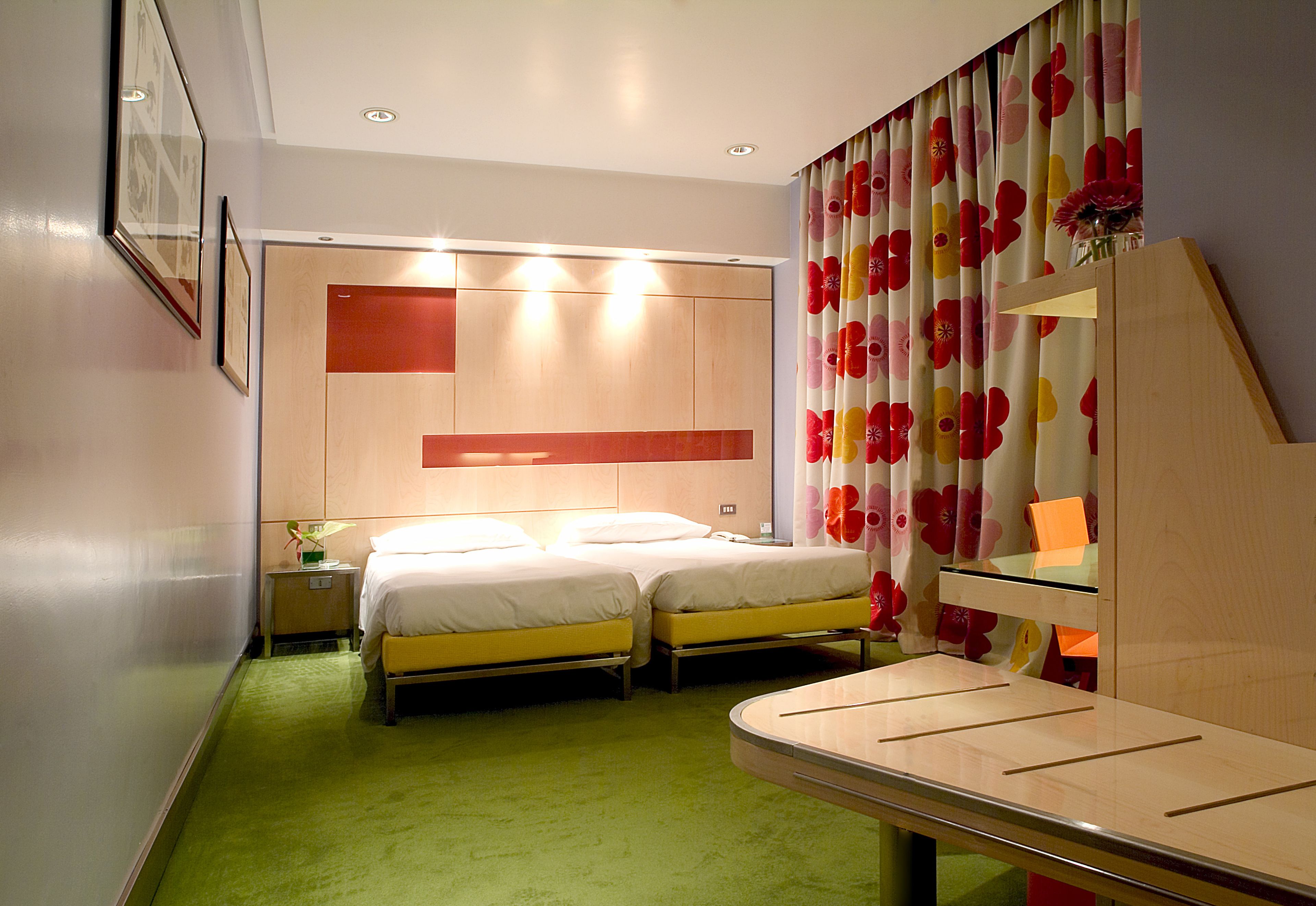 Ein Hotelzimmer mit zwei Betten, einem kleinen Nachttisch, einem Spiegel und einem grünen Teppich.