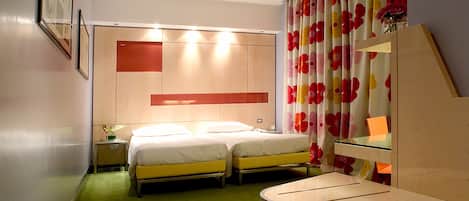 A hotel room with two beds, a small bedside table, a mirror, and a green carpet.