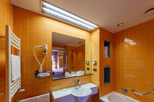 A bathroom with orange tiles, a white sink, a glass shelf with toiletries, a mirror, and a shower area.