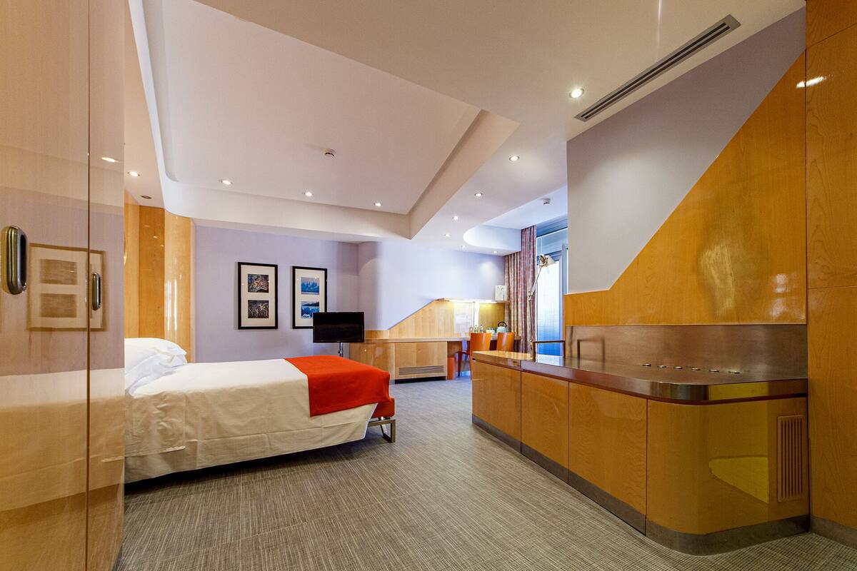A hotel room with a bed, a desk, a chair, a TV, and a bathroom.