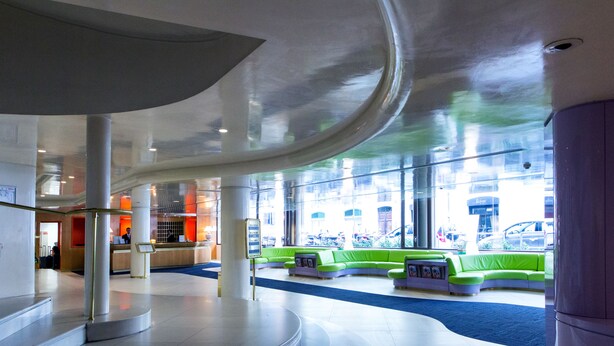 A modern lobby with a curved ceiling, a reception desk, and green seating areas.