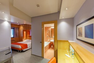 Una camera d'albergo con due letti, un bagno, una scrivania con uno specchio e un quadro appeso al muro.