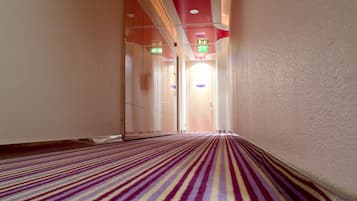 Un couloir d’hôtel avec un tapis à rayures, des portes en verre et des panneaux indiquant les sorties de secours.