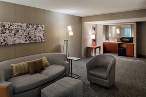 Relax in this stylish space with a comfortable sofa, armchair, and floor lamp, plus a compact kitchenette and large abstract art piece.