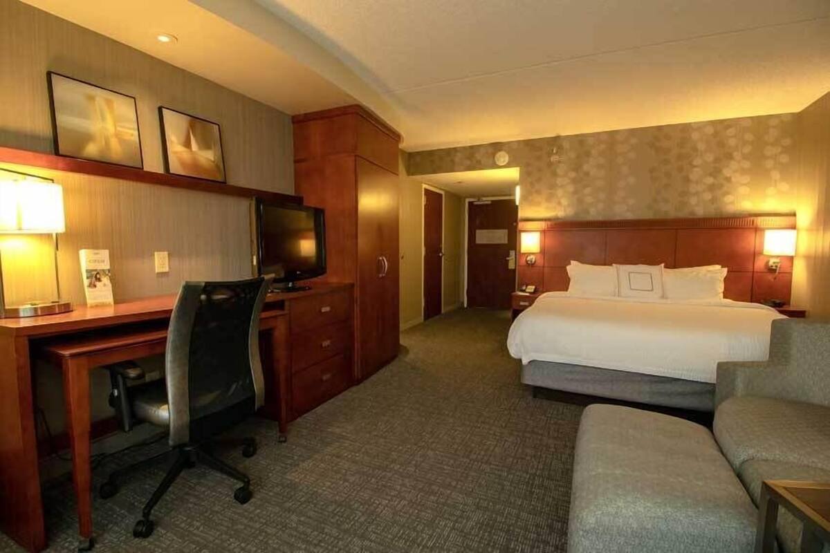 A hotel room with a bed, desk, chair, TV, and a small table.