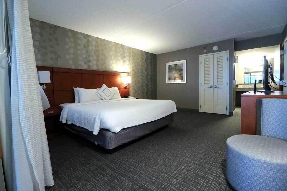 A hotel room with a bed, a desk, a chair, a wardrobe, and a bathroom.