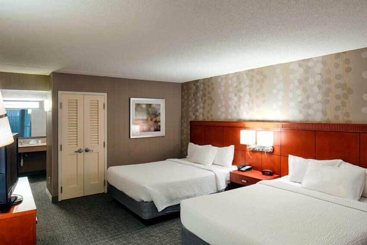 A hotel room with two beds, a desk, a chair, a TV, a phone, and a door.