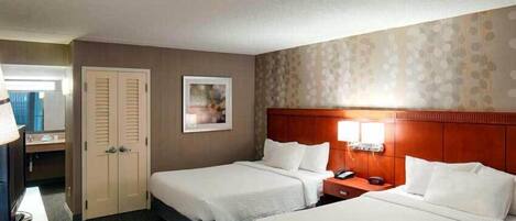 A hotel room with two beds, a desk, a chair, a TV, a phone, and a door.