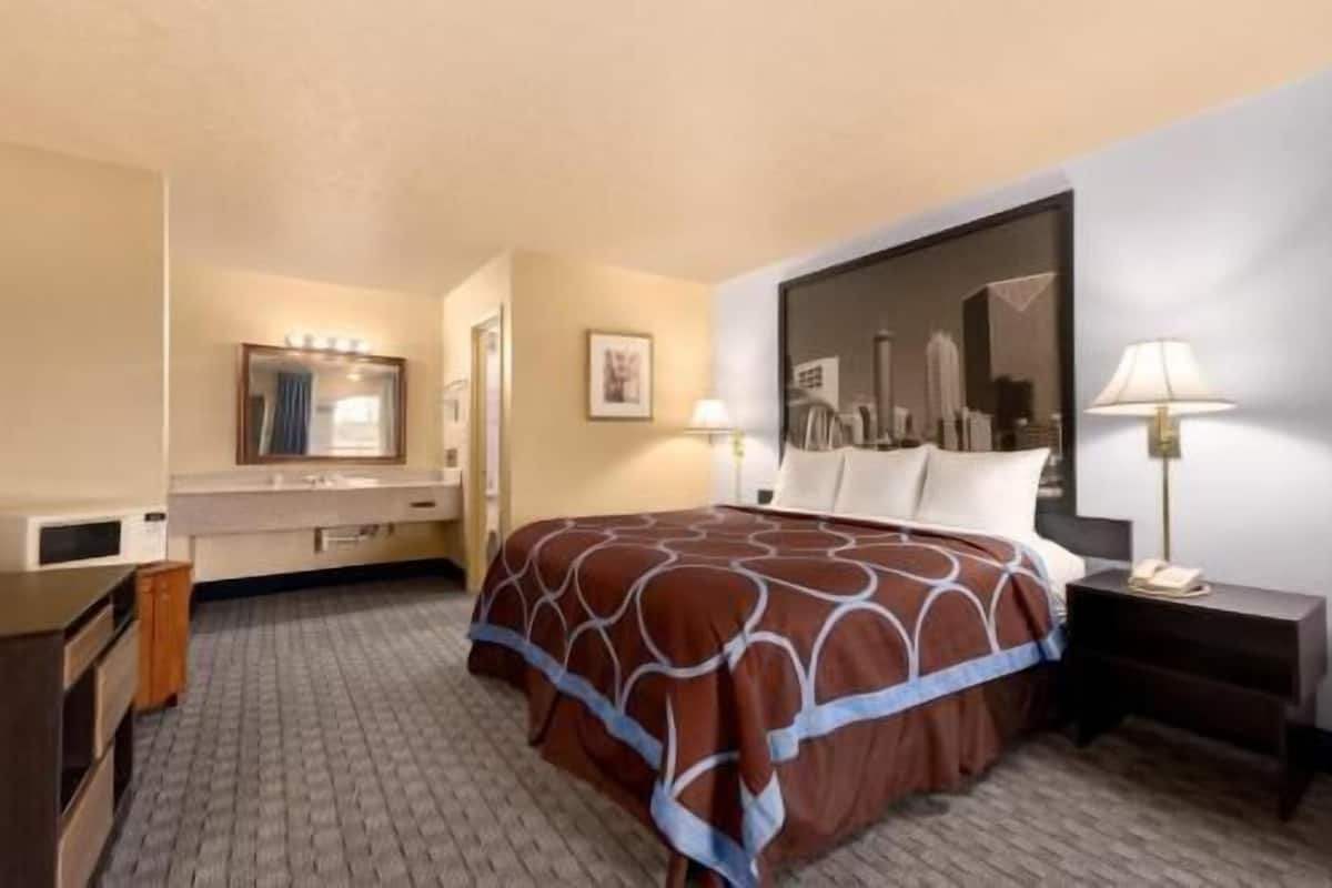 A hotel room with a bed, a desk, a chair, a mirror, and a nightstand.