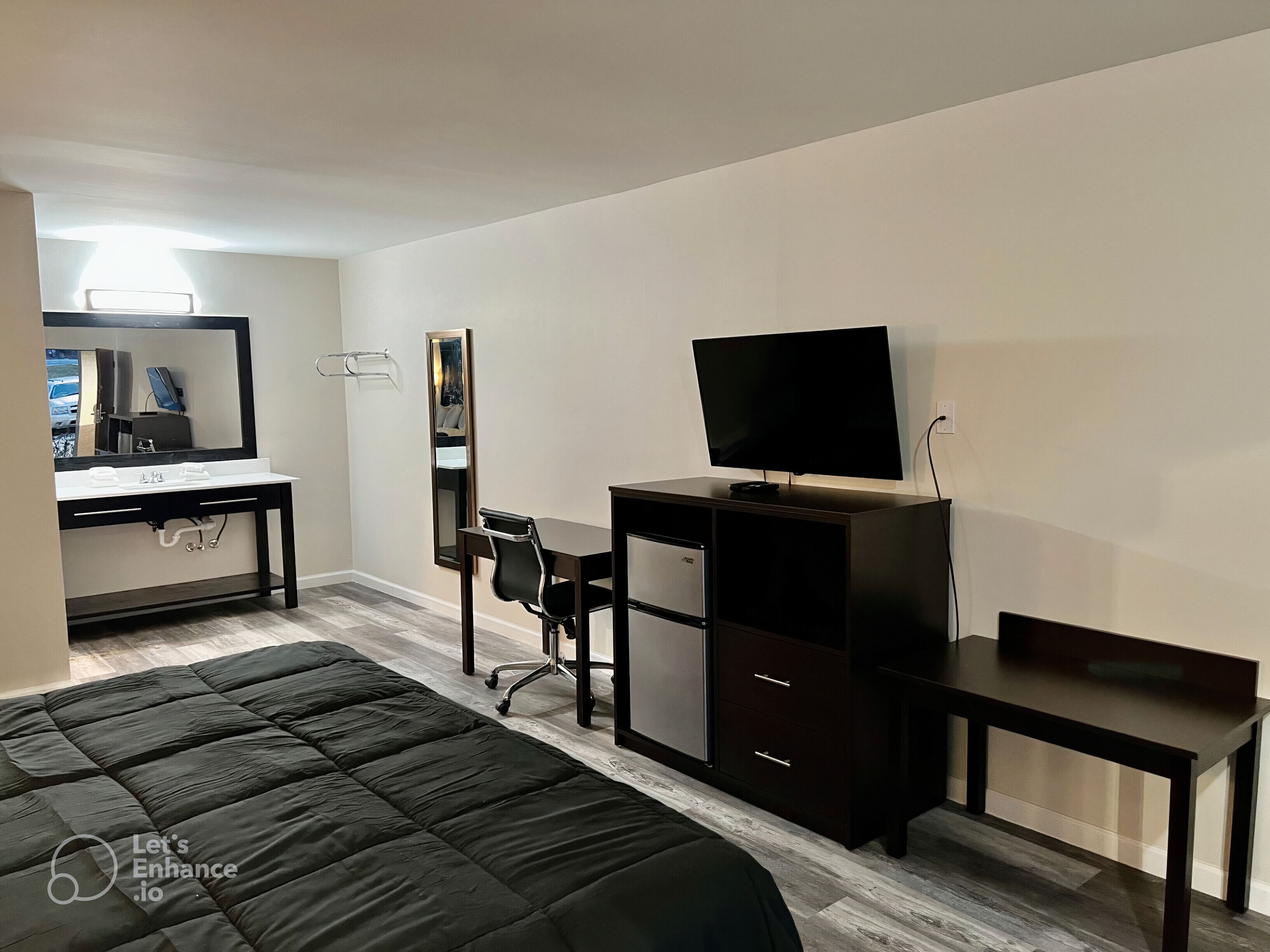 A modern hotel room with a bed, a desk, a chair, a TV, and a wardrobe.