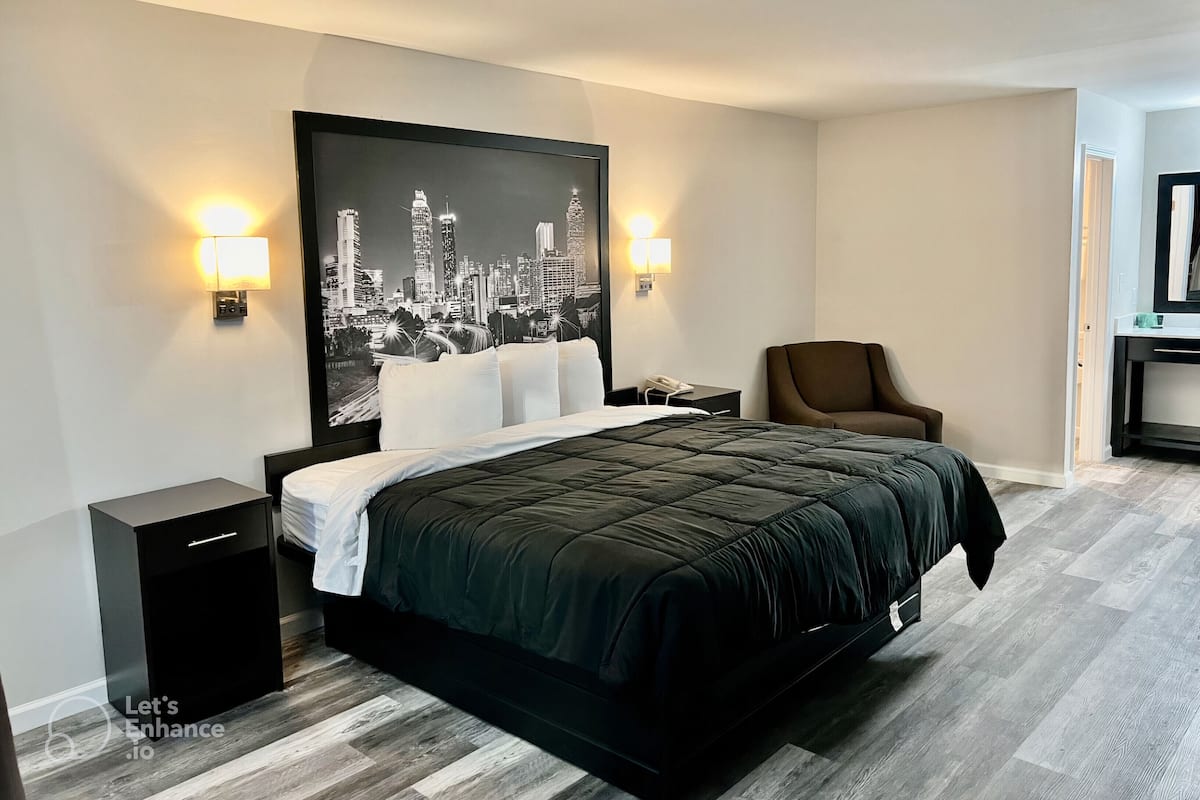 A modern hotel room with a large bed, a cityscape artwork on the wall, two bedside lamps, a chair, and a small table with a phone.